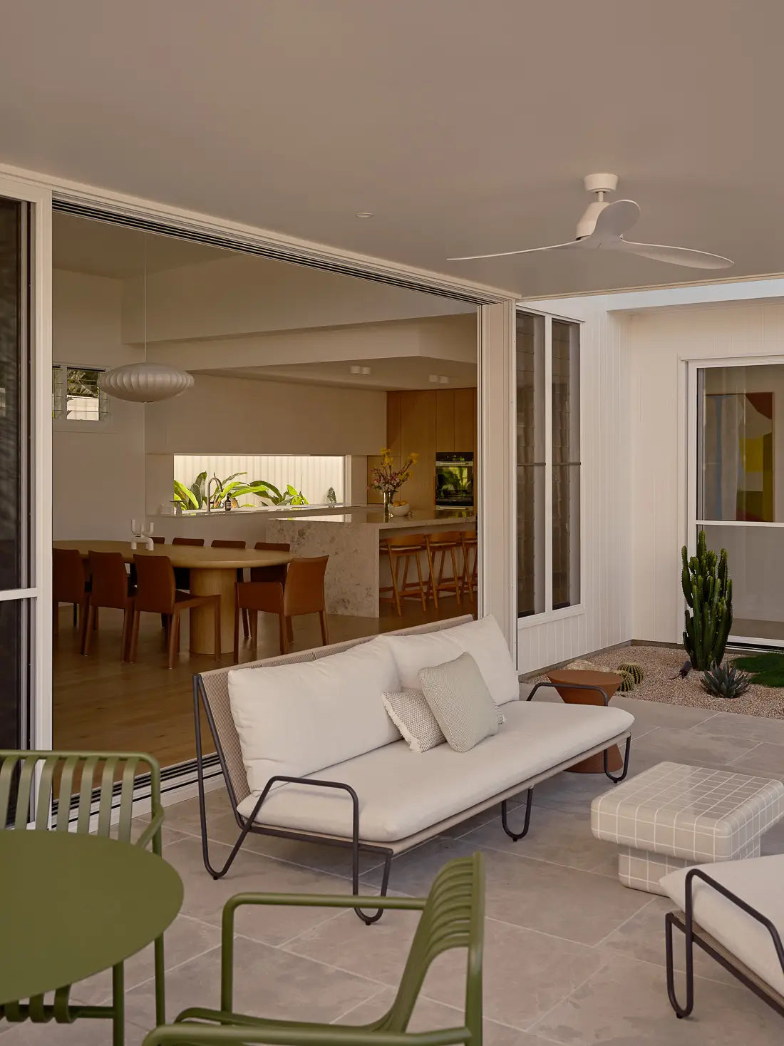 Modern patio with white outdoor sofa looking into open dining and kitchen area.