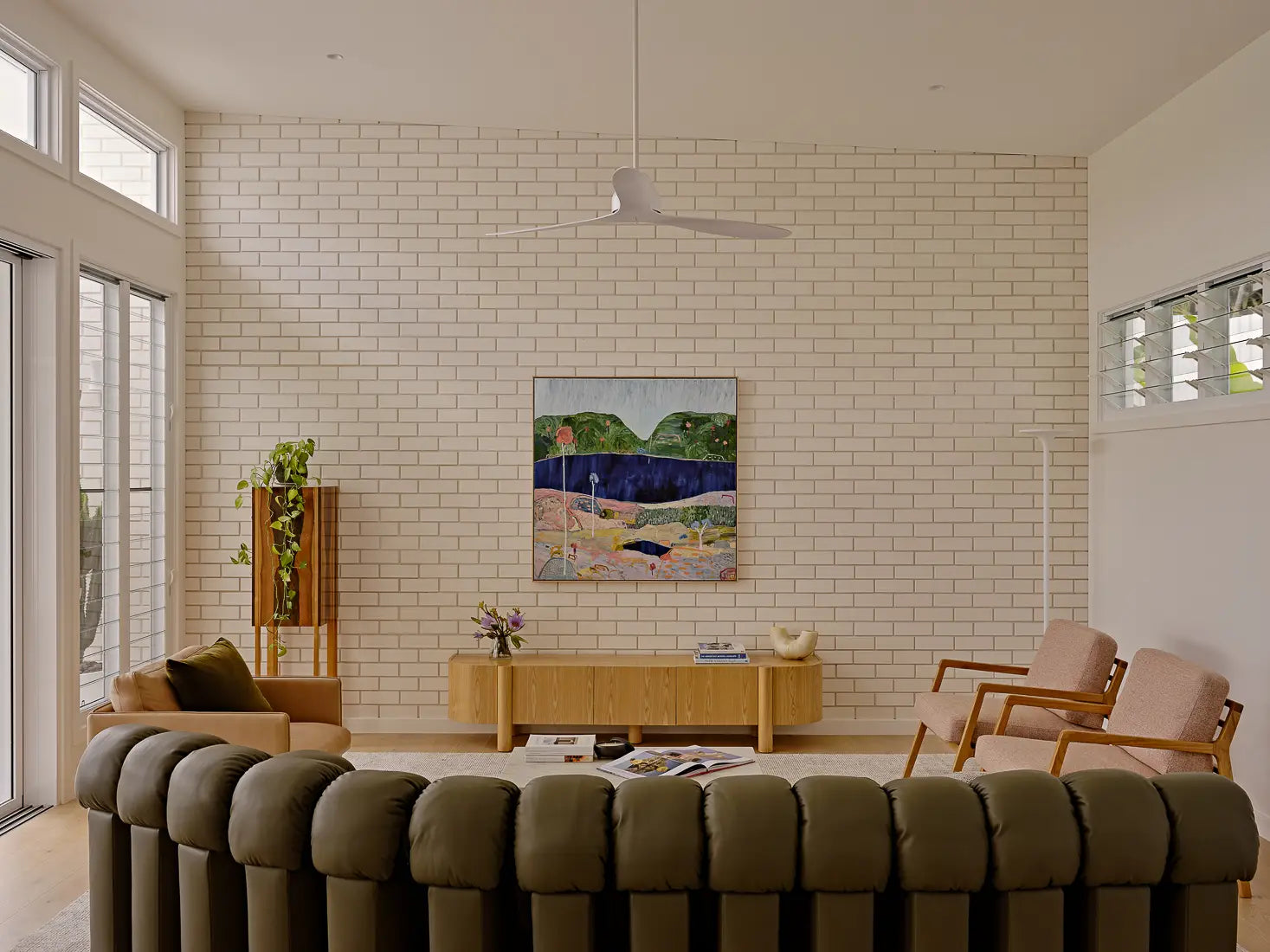 Bright living room with white brick wall, green curved sofa, and colorful abstract painting.