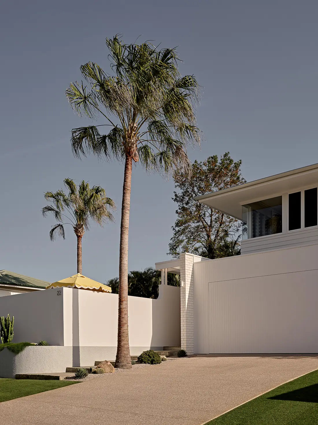 Exterior of a modern white house with a tall palm tree and gravel driveway.