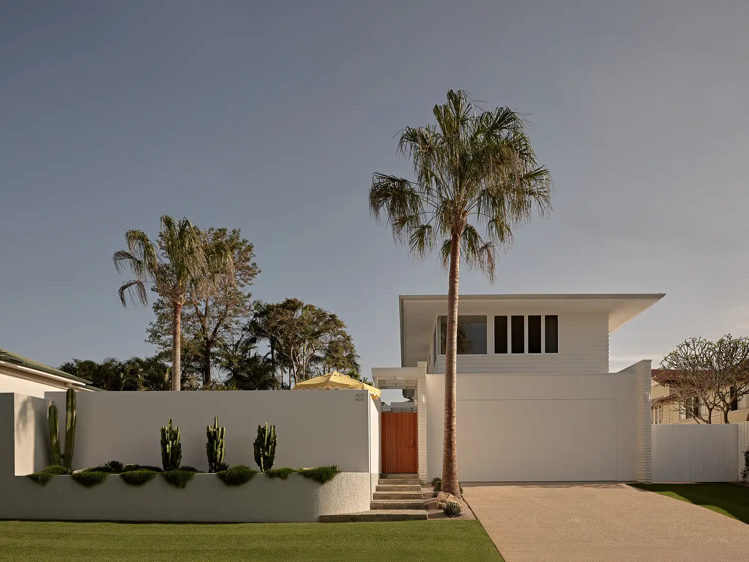 Front view of a stylish white house with palm trees, cacti, and a green lawn.