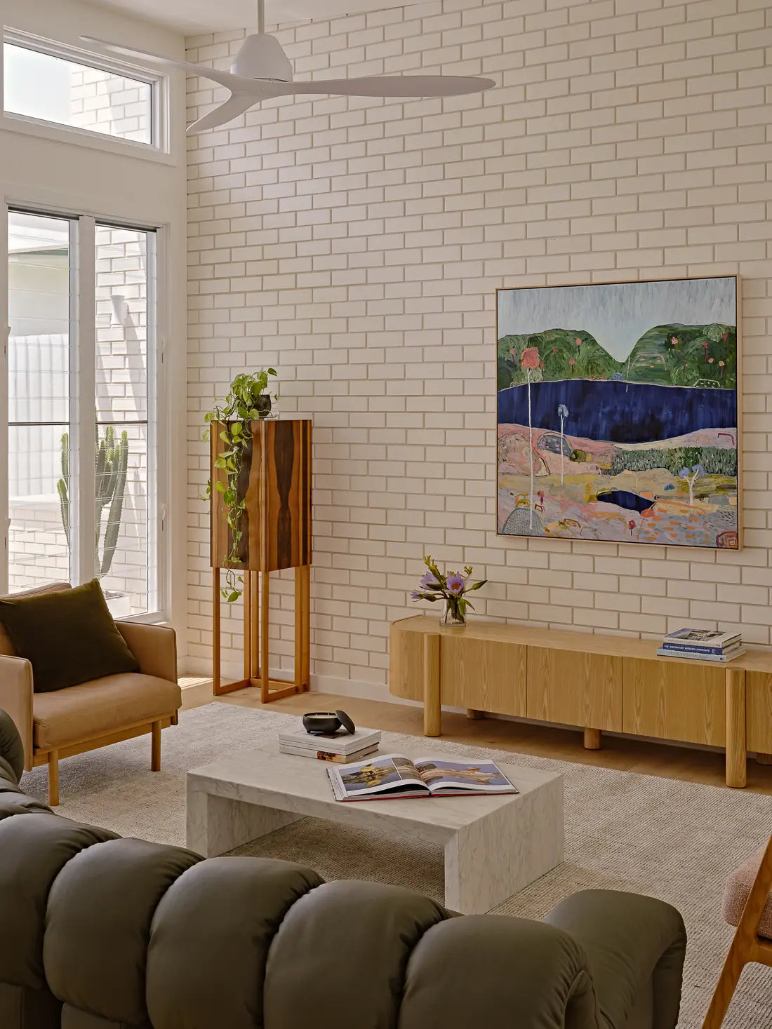 Contemporary living room with a deep green leather sofa, marble table, and large landscape art.