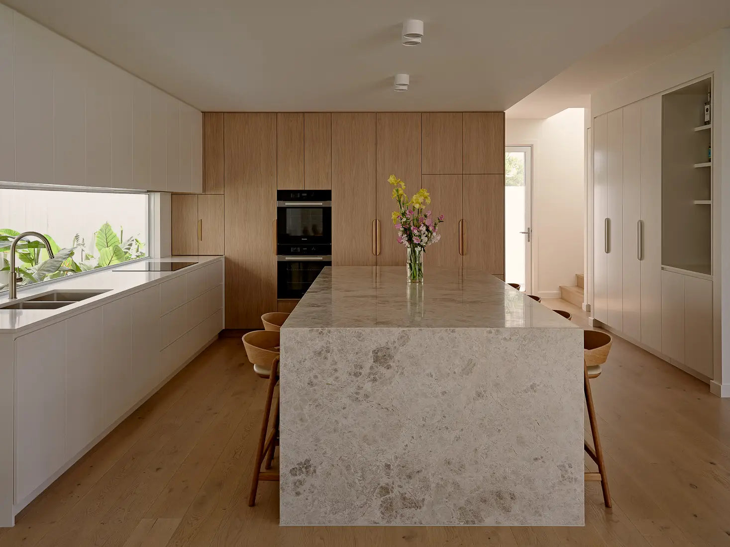 Sleek modern kitchen with light wood cabinets, white countertops, and a marble island.