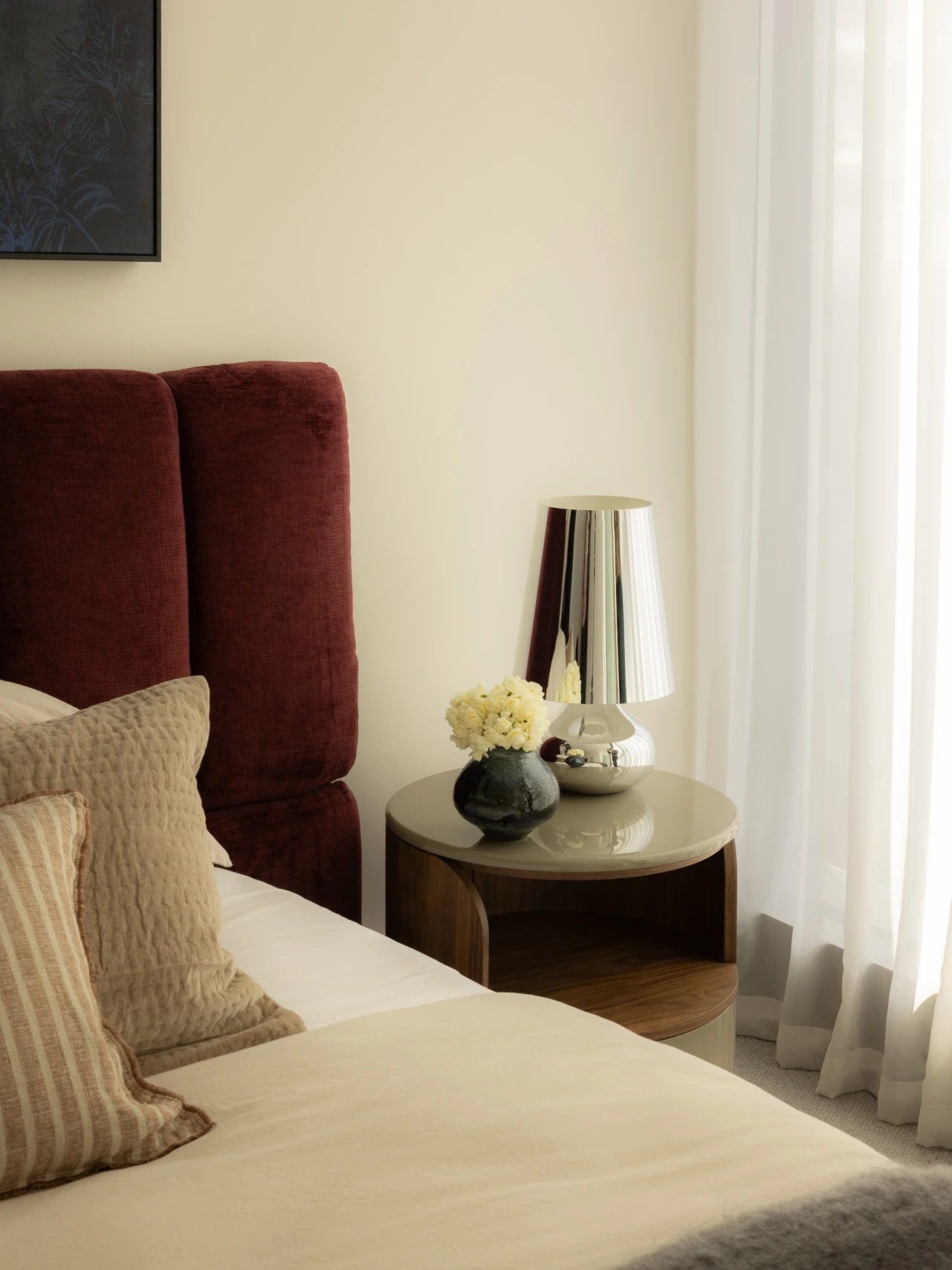 Bedroom with a red headboard, pillows, and a side table with a lamp and flowers.